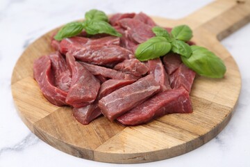 Pieces of raw beef meat and basil on white marble table, closeup