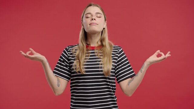 Tranquil woman relaxing, meditating, refuses stress. Young lady breathes deeply, calms down, Red studio background. Yoga, moral balance, zen concept.