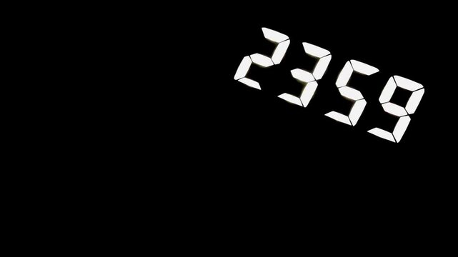 A digital clock switching from 23:59 to 00:00 in a dark room