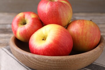 Ripe red apples in bowl on wooden table, closeup