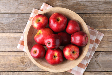 Ripe red apples in bowl on wooden table, top view