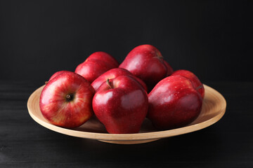 Ripe red apples on wooden table against black background, closeup