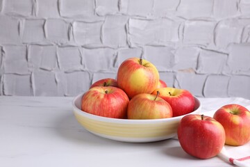 Ripe red apples and bowl on white table near grey textured wall, closeup. Space for text