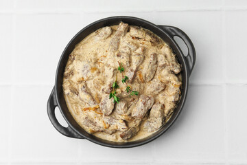 Tasty beef Stroganoff with thyme in baking pan on white tiled table, top view