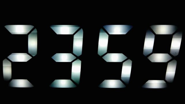 A digital clock switching from 23:59 to 00:00 in a dark room