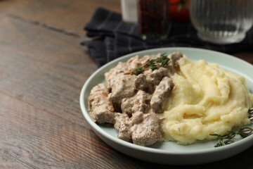 Delicious beef stroganoff with mashed potatoes and thyme served on wooden table, closeup. Space for text