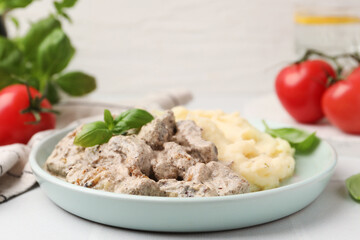 Delicious beef stroganoff with mashed potatoes and basil served on white tiled table, closeup. Space for text