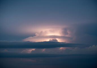 A dramatic evening sky filled with dark, ominous storm clouds illuminated from within by a powerful flash of lightning