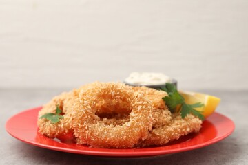 Deep fried squid rings with parsley, sauce and slice of lemon on grey textured table, closeup. Space for text
