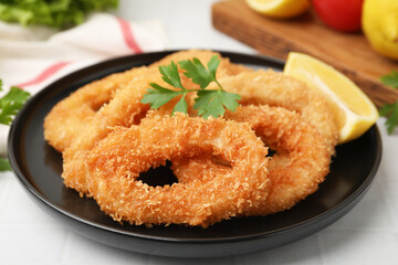 Deep fried squid rings with parsley and lemon slice on white tiled table, closeup