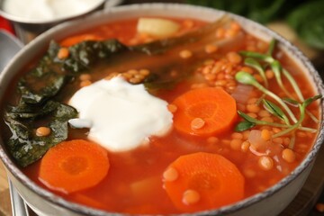 Tasty lentil soup with sour cream in bowl on table, closeup