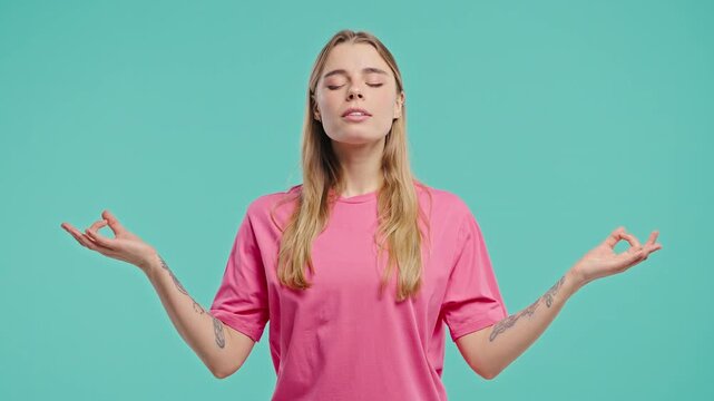 Tranquil woman relaxing, meditating, refuses stress. Young lady breathes deeply, calms down, Blue studio background. Yoga, moral balance, zen concept.