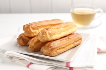 Tasty eclairs and tea on white table, closeup