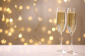 Merry Christmas and Happy New Year. Flute glasses with sparkling wine on white table against blurred lights. Space for text