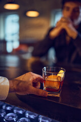 Bartender sliding amber drink toward thoughtful customer at bar. Concept of crafted cocktails, drink presentation, relaxed evening atmosphere, and emotional beverage storytelling.