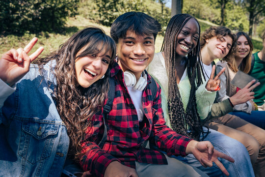 Joyful multicultural group of young students taking a cheerful selfie outdoors, smiling together during a sunny day in the park.