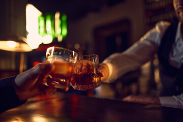 Hands clicking whiskey glasses in warm bar light. Concept of drink promotion, social bar gatherings, nightlife advertising, premium beverage branding, and event-focused visuals.
