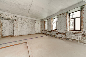 Spacious empty room under renovation with whitewashed brick walls, high ceiling and large modern windows