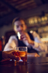 Hand holding glass of amber drink at bar counter. Concept of bar service workflow, relaxed end-of-day routine, beverage order moments, and crafted drink presentation.