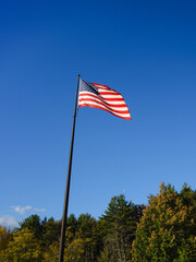 American flag, also called Stars and Stripes, Old Glory or Star-Spangled Banner flying in the sunlight against clear blue sky in Maine, USA, symbol for freedom and patriotism