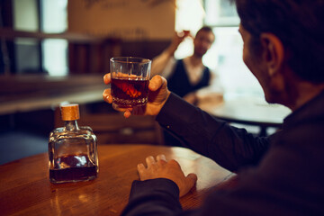 Man raising whiskey glass toward man in background. Concept of casual bar meetings, loyalty program visuals, nightlife atmosphere ads, and beverage-centered social marketing.