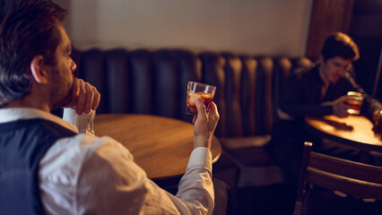 Men holding classic drinks at small table in dim lounge. Concept of quiet unwind, after-work relaxation, slow-paced bar atmosphere, and casual beverage enjoyment.