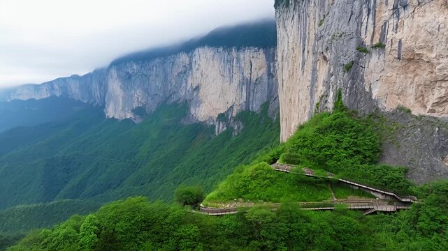 Ascending mountain path along sheer cliff face with forest below