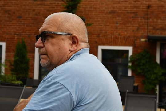 An elderly man wearing glasses and a blue polo shirt on a city street. - Powered by Adobe