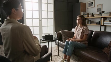 Brunette mental health specialist explaining young woman how to do breathing exercise during counselling session in modern office