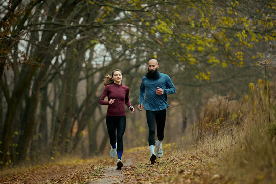 Active runners moving forward on forest trail in crisp autumn season. Concept of outdoor vitality, functional fitness, lifestyle motivation, healthy habits and seasonal wellness engagement. - Powered by Adobe