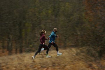 Fototapeta premium Runners in dynamic stride captured with long-lens blur on autumn trail. Concept of athletic motion, outdoor performance, lifestyle fitness, seasonal energy and healthy active habits.