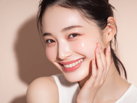 笑顔できらめく綺麗な肌に美容クリームを塗る日本人女性美人モデルの接写写真。スキンケア、コスメ、ビューティーケア広告用