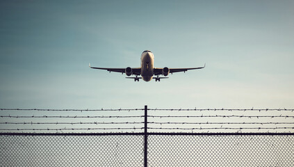 A commercial airplane soaring above a fence with barbed wire, capturing aviation and travel themes.