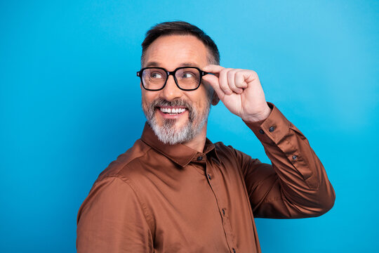 Fototapeta Confident mature businessman adjusts his glasses during a stylish corporate photo shoot in a bright blue studio