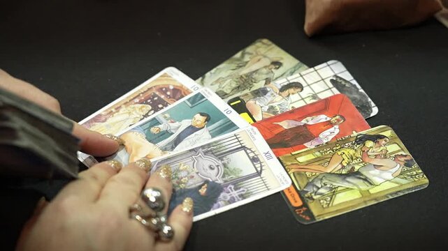 Tarot reader arranges cards across deep black cloth creating focused atmosphere. Reader performs detailed card layout over smooth surface
