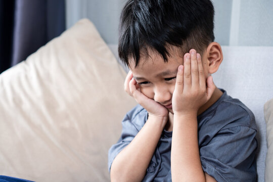 Asian boy with toothache, headache, and gum pain, holding his cheek with both hands while feeling frustrated and uncomfortable. 