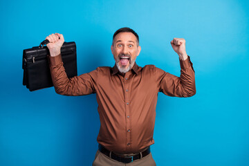 Confident mature businessman celebrates success with briefcase in blue studio background for corporate stock image