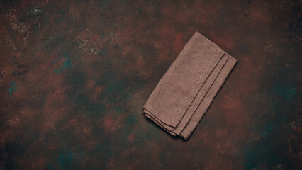 Brown linen napkin on dark rusty grunge background, top view, flat lay, copy space, culinary backdrop