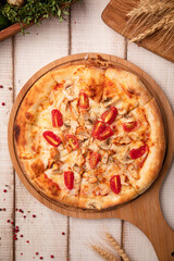 Hot chicken pizza topped with cherry tomatoes, cheese and spices on a wooden board