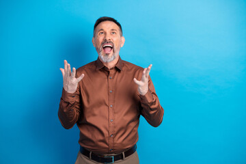 Confident mature businessman in brown shirt expresses excitement gesturing with open hands against...