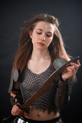 Obraz premium Portrait of a young woman, fantasy warrior in armor with a sword in her hands isolated on a dark background.