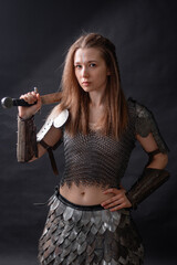 Obraz premium Portrait of a young woman, fantasy warrior in armor with a sword in her hands isolated on a dark background.