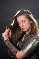 Obraz premium Portrait of a young woman, fantasy warrior in armor with a sword in her hands isolated on a dark background.