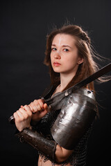 Obraz premium Portrait of a young woman, fantasy warrior in armor with a sword in her hands isolated on a dark background.
