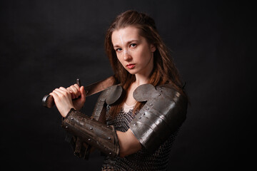 Obraz premium Portrait of a young woman, fantasy warrior in armor with a sword in her hands isolated on a dark background.