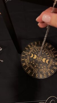 Pendulum over a spirit board on a wooden table with candles esoteric occult divination ritual, mystical altar, magical tools, fortune telling setup