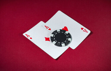 Two ace playing cards lie on a smooth red surface with a black and white poker chip placed on top. This scene captures the excitement of a casino game, showcasing high stakes