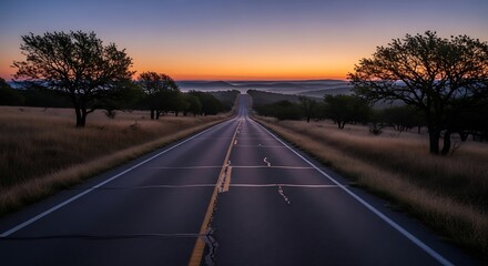 A lonely road stretches through dry grass and trees at sunrise.