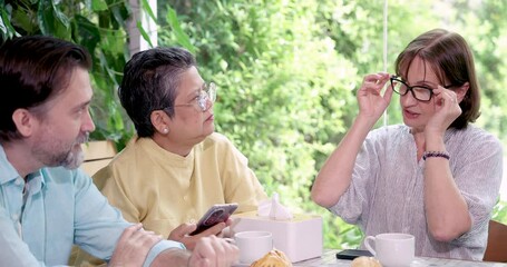 Senior asian woman looking at smartphone while sitting with senior caucasian man at cafe table during casual retirement meetup surrounded by tea pastry and meaningful lifestyle connection
