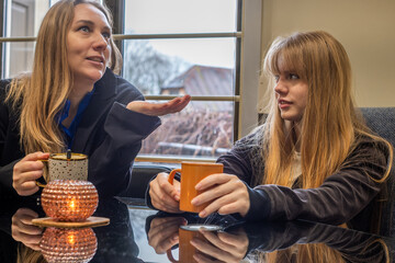 Mother and daughter enjoying warm beverages together at a cozy table, sharing stories and laughter, highlighting their close family relationship and togetherness